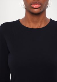 Navy blue, fitted long-sleeve top with a round neck. Smooth texture and minimal design with no visible logos or patterns.