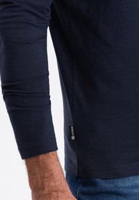 T-paita, jossa on pitkät hihat merivoimien sinisessä värissä, valmistettu puuvillasta. Se on slim fit -mallinen, hihansuissa on rypistymistä ja alareunassa on pieni etiketti.