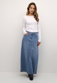 Long denim skirt in light blue with a straight cut, front seam detail, and pockets. Paired with a fitted white long-sleeve top and black boots.