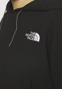 Felpa con cappuccio nera realizzata in tessuto testurizzato, con un piccolo logo bianco The North Face sul petto e coulisse con punte nere.
