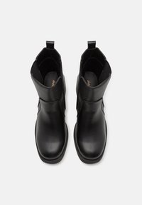 Mustat nahkaiset nilkkurit, joissa on teksturoitu musta yläosa, liukumasuunnittelu, pyöreä kärki ja pienet vetotabut. Liukas pinta, jossa on hienovaraisia yksityiskohtia.