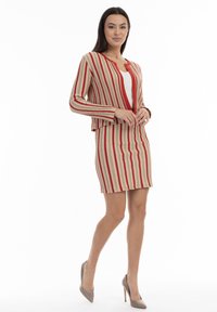 Randig tvådelad outfit med en röd och beige färgskala, strukturerat tyg, figursydd design och en kort jacka med hänge.