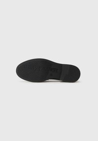 Sole di scarpa nera con un motivo di grip testurizzato e logo in rilievo. Il materiale sembra gomma con una forma arrotondata e un profilo piatto.