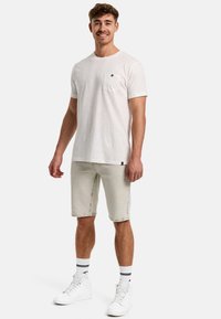 Hvid bomulds T-shirt med brystlomme, parret med lysegrå denimshorts. Båret med hvide sneakers og mønstrede sokker. Afslappet pasform.