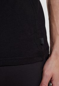 Sort kortærmet T-shirt, blødt bomuldsstof, tætsiddende design, har et lille mærke på sidesømmen, glat tekstur.