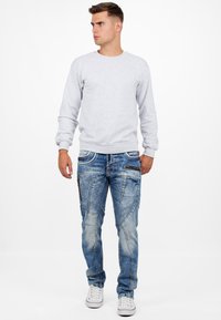 Felpa grigia a girocollo, jeans blu con motivo e zip, e sneakers bianche. L'outfit ha un fit e un design casual e moderno.