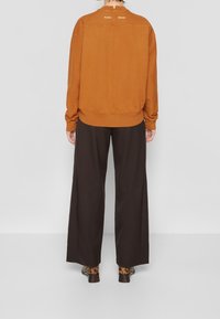 Brown sweatshirt with ribbed cuffs and hem, featuring two white text elements on the back; paired with wide black pants and patterned ankle boots.