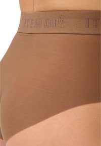 Braune hochgeschnittene Shorts mit glatter Textur und elastischem Bund, der das erhabene Logo-Design "ITEM m6" zeigt.