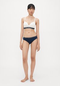 White push-up bra with black logo band and matching navy bikini briefs featuring logo waistband, both made of smooth fabric.