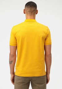 Geel poloshirt met een klassieke kraag en korte mouwen, met een gladde textuur en een rechte zoom. Minimalistisch ontwerp, zonder versieringen.