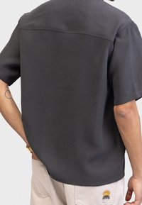 Kurzarmhemd in Dunkelgrau mit glatter Textur, entspannter Passform und minimalistischem Design. Die Rückansicht zeigt keine markanten Muster oder Akzente.