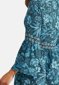 Robe floral en vert canard foncé avec des motifs floraux détaillés en bleu clair. Dotée de manches cloche et d'une ceinture texturée à motifs.