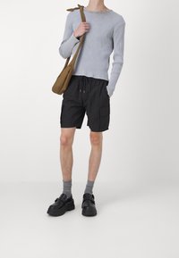 Haut long à manches ribbées gris, shorts cargo noirs avec poches latérales, chaussettes mi-hautes grises et chaussures noires avec une semelle épaisse et un détail de boucle.
