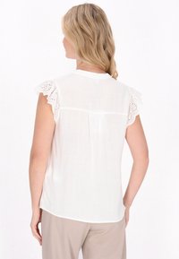 Bluză albă cu mâneci scurte, volanate, având detalii din dantelă, material ușor și un design plisat la spate.