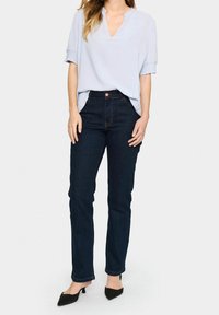 Blusa azzurra chiara a maniche corte con scollatura a V, abbinata a jeans in denim blu scuro con vestibilità slim e cuciture a contrasto. Tacchi neri.