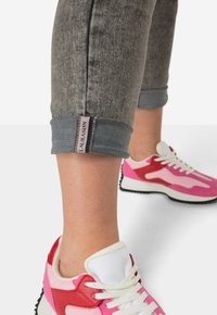 Pantalones cortos de mezclilla gris con dobladillos vuelta, que presentan una etiqueta, combinados con zapatillas deportivas multicolores en tonos de rosa y rojo.