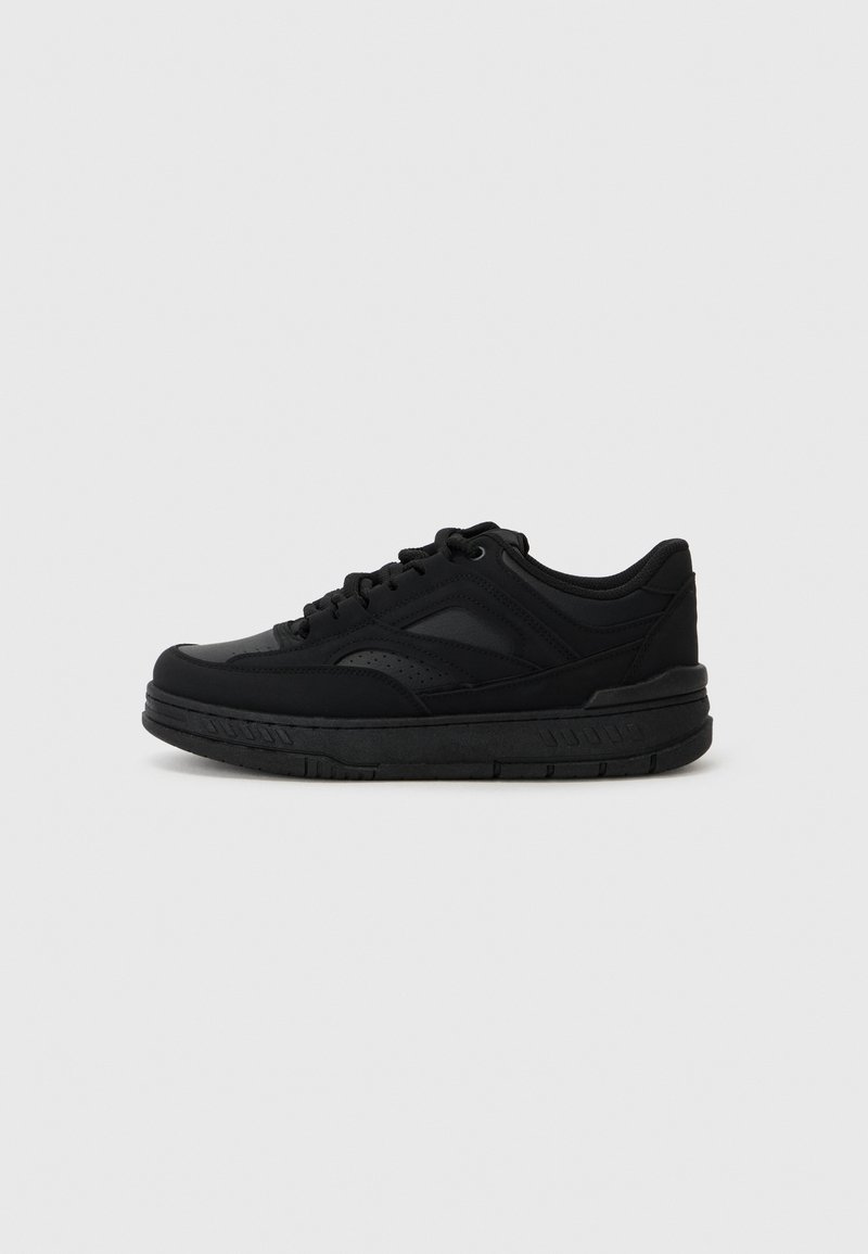 Black athletic shoe made of synthetic materials. Features a rounded toe, flat sole, and textured accents on the upper and sides.