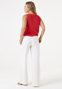 Rotes, geripptes, ärmelloses Top mit lockerer Passform, kombiniert mit weißen, weit geschnittenen Hosen. Das Outfit zeichnet sich durch ein dezentes Detail auf der Rückseite und eine glatte Textur aus.