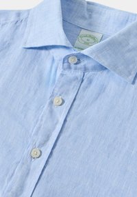 Chemise en lin bleu clair avec un col pointu, trois boutons et une finition texturée. Comprend une étiquette indiquant la taille M.