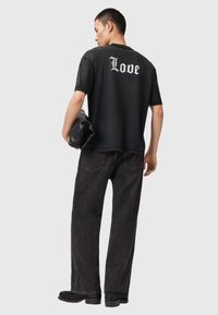 Fekete pamut póló, hátsó részén fehér gótikus betűkkel "Love" felirattal. Laza fazonú fekete farmernadrággal és csizmával párosítva.