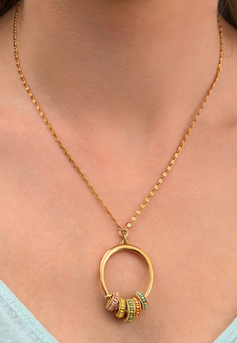 Collier ton doré avec un pendentif circulaire orné d'anneaux multicolores et d'une chaîne texturée, sur fond neutre.