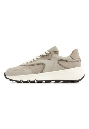 Lichtgrijze sneaker met suède en geperforeerde leren panelen, witte veters, dikke witte zool en zwart profiel op een witte achtergrond.