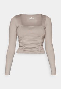 Långärmad beige topp med rynkad textur, fyrkantig halsringning och figurbetonad design. Tillverkad av mjukt, stretchigt tyg.