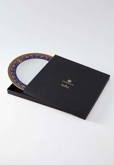 Versace dekoratīvs šķīvis eleganti melnā kastē. Šķīvja mala ir rotāta ar detaļām zelta un zilā krāsā, un centrā ir caurspīdīgs laukums.