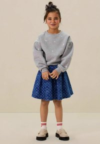 Sweat-shirt gris avec broderie florale, associé à une jupe bleue présentant une texture à motifs. Complété par des chaussettes blanches et des chaussures noires.