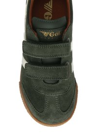 Zapatilla de ante verde con rayas blancas, correas de velcro y suela de goma marrón. Presenta un logo dorado sobre un fondo verde oscuro.