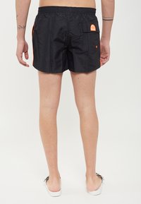 Pantaloni da nuoto neri con cintura elastica, tasche laterali e una tasca posteriore con un logo e dettagli arancioni brillanti. Texture liscia.