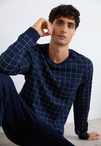 Chemise à manches longues bleu marine avec un motif à carreaux, dotée d'un col rond et d'une poche sur la poitrine. Texture douce, portée avec un pantalon sombre assorti.
