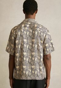 Cămașă cu mânecă scurtă de culoare crem, cu un model geometric în valuri bleumarin. Dispune de un guler clasic și o croială lejeră, fiind fabricată dintr-un material ușor.