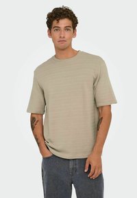 Korte mouw beige t-shirt met een gestructureerd patroon, ronde halslijn, relaxte pasvorm, gecombineerd met grijze jeans.