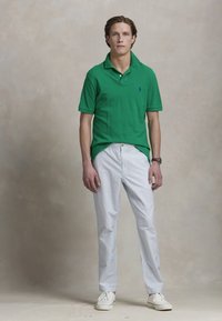 Polo verde in cotone a maniche corte, abbinato a pantaloni a righe blu chiaro e bianche. Sneakers bianche completano l'outfit.