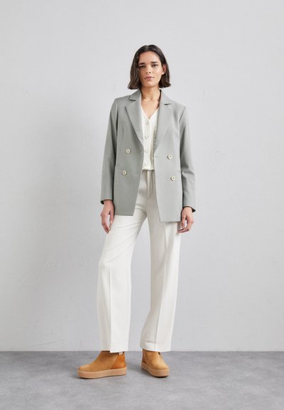 Light grey double-breasted blazer, white buttoned top, white trousers, and tan platform ankle boots. Smooth fabric with a tailored fit.