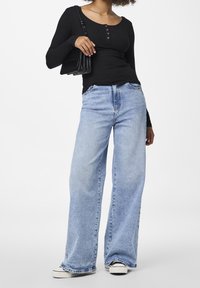 Svart ribbad långärmad topp med tre knappar; ljusblå vida jeans; svart axelväska; vita sneakers med svarta detaljer.