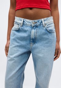 Τζιν παντελόνι μέσης σε ανοιχτό μπλε χρώμα, φορεμένο από άτομο με καστανό δέρμα, συνδυασμένο με κόκκινο κοντό τοπ.