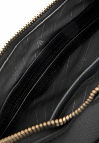 Intérieur d'un sac à main en cuir noir avec une fermeture éclair dorée. Comprend plusieurs compartiments et un revêtement en tissu texturé avec des rayures diagonales.