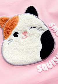 Pink shirt featuring a textured, plush cat face design with orange, white, and black fur accents and playful "SQUISHY" lettering.