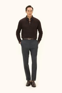 Brauner Strickpullover mit halbem Reißverschluss, graue maßgeschneiderte Hose, brauner Gürtel und dunkelbraune Schuhe. Das Model steht mit den Händen in den Taschen.