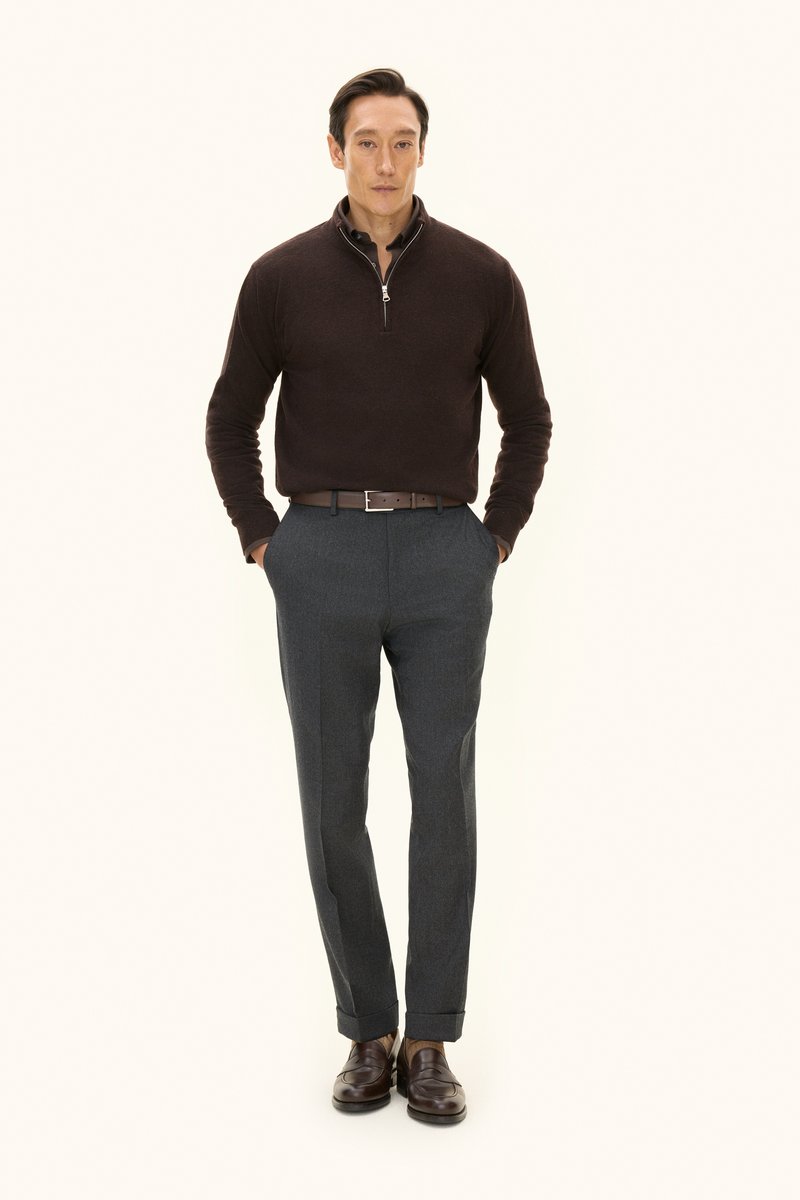 Brown knit sweater with half-zipper, gray tailored trousers, brown belt, and dark brown shoes. Model stands with hands in pockets.
