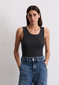 Zwarte, geribbelde tanktop met een ronde hals en een klein logo. Gecombineerd met high-waisted, lichtblauwe denim jeans met zijzakken.