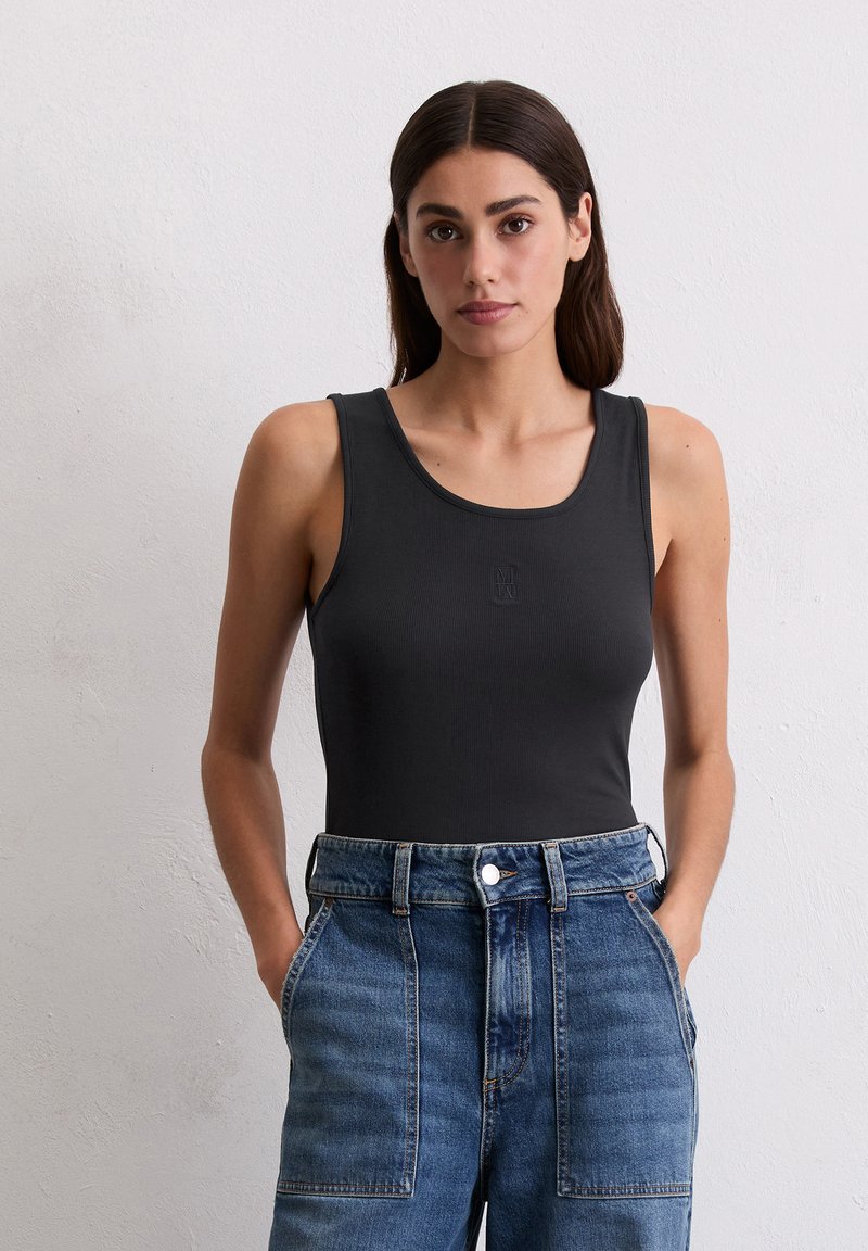 Zwarte, geribbelde tanktop met een ronde hals en een klein logo. Gecombineerd met high-waisted, lichtblauwe denim jeans met zijzakken.