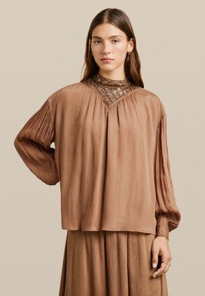 Blusa marrone plissettata con un collo alto e lavorato e maniche lunghe, realizzata in tessuto leggero. Texture liscia, vestibilità comoda.