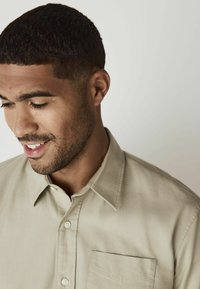 Beige overhemd met korte mouwen en een knoopsluiting, voorzien van een borstzak aan de linkerkant, met een klassieke kraag en een gladde, gestructureerde stof.