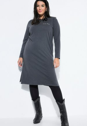 Kvinde iført en mørkegrå midi-kjole med lange ærmer og teksten "easy day", sorte leggings og sorte cowboystøvler med nitter.