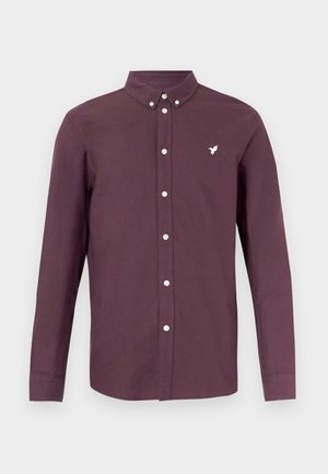 Langærmet skjorte med knapper i dyb bordeauxstof, med en hvid broderet logo og en knaplukket krave. Glat tekstur.