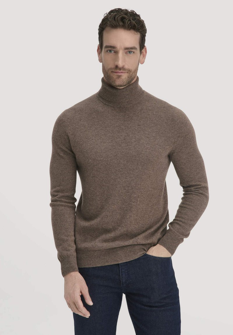 Brauner Rollkragenpullover mit langen Ärmeln, geripptem Kragen und Bündchen, aus einem weichen, strukturierten Stoff gefertigt. Getragen mit dunkelblauen Jeans.