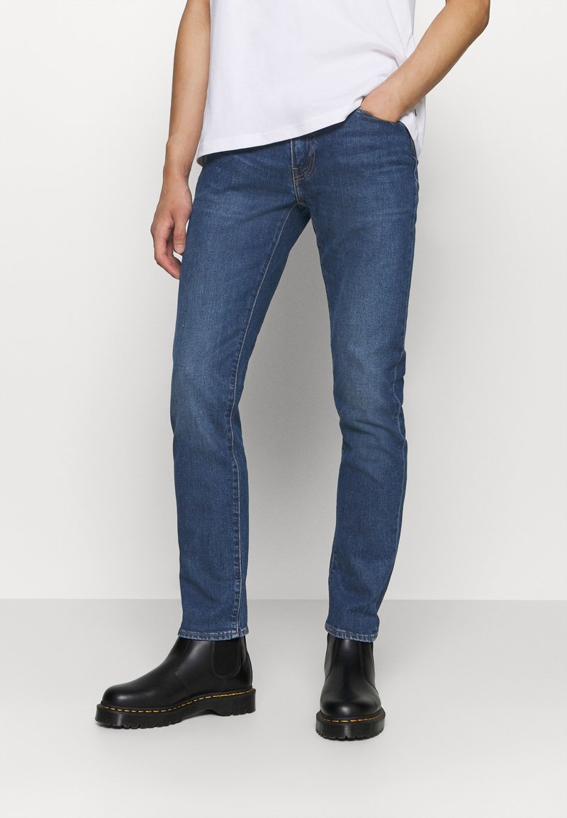 Mörkblå denimjeans med smal passform, med midja i mitten och minimalistisk design. Kombinerade med svarta läderstövletter.